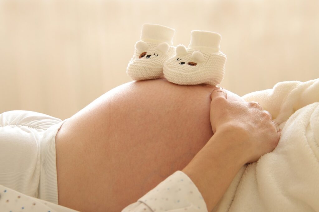 Geburtshilfe, Bauch einer schwangeren Frau mit Babyschuhen